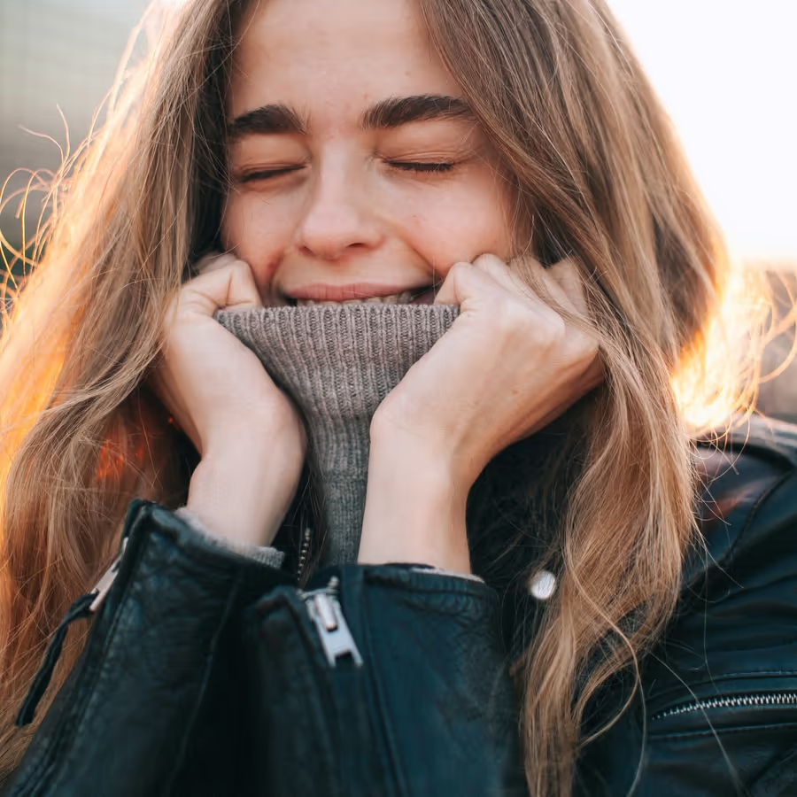 Веселая девушка прячет лицо в воротник свитера