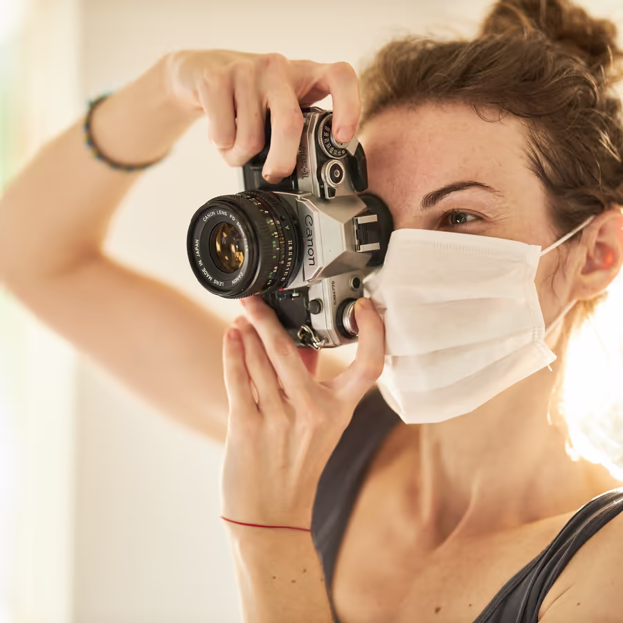 Девушка-фотограф делает снимок используя пленочную камеру и медицинскую маску