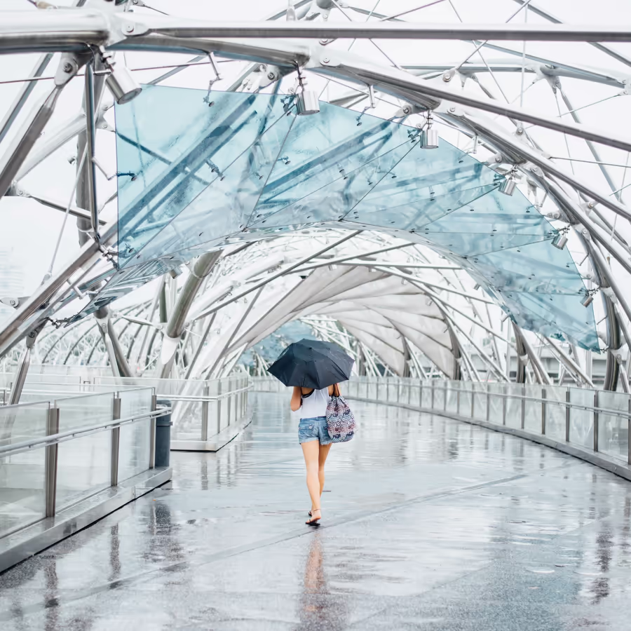 Девушка с зонтом идет по мосту Геликс в Сингапуре во время дождя