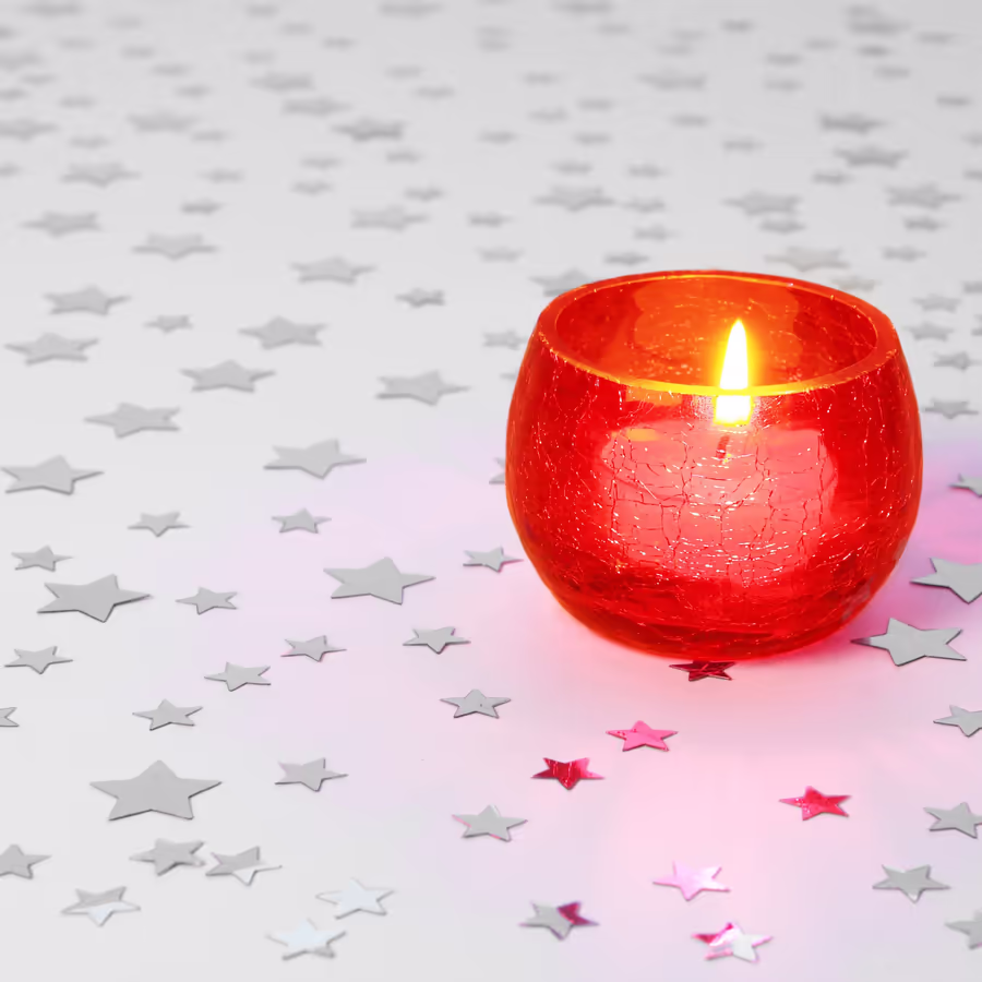 Зажженная красная свеча окружена блестящей серебряной и розовой звездной конфетти