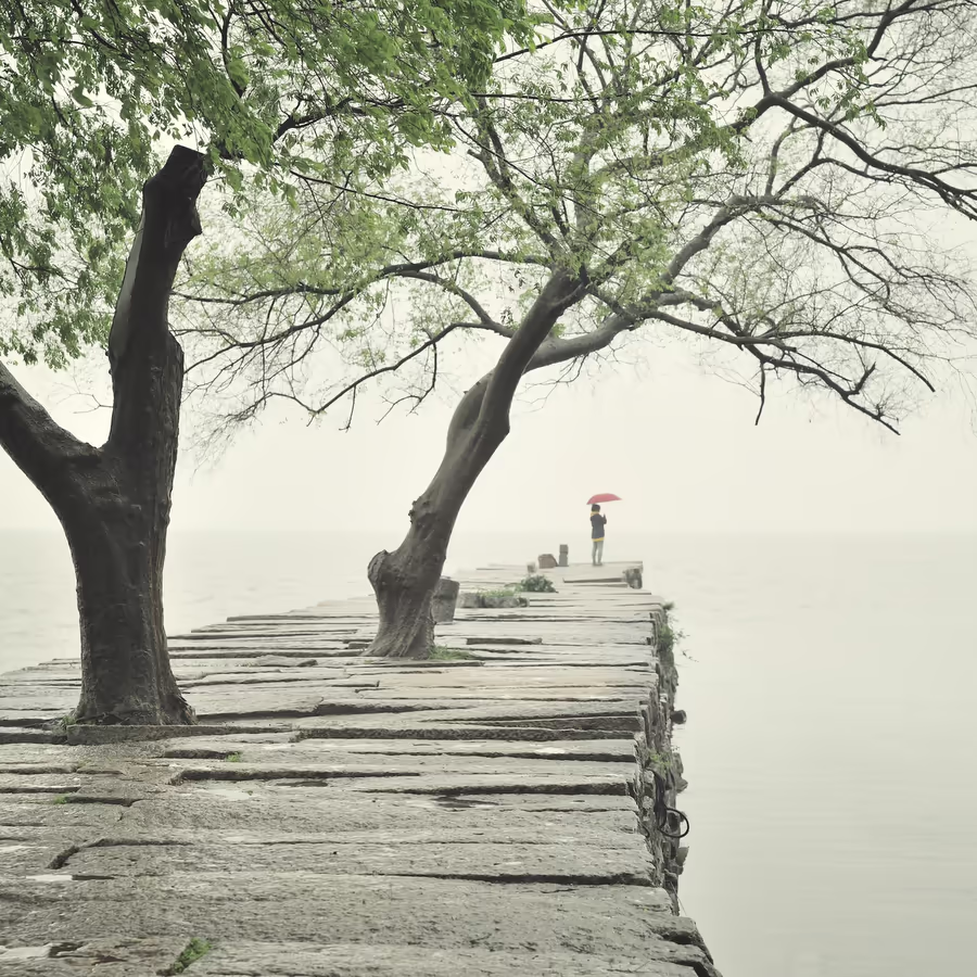 Человек с красным зонтом стоит в одиночестве на пирсе в туманный день
