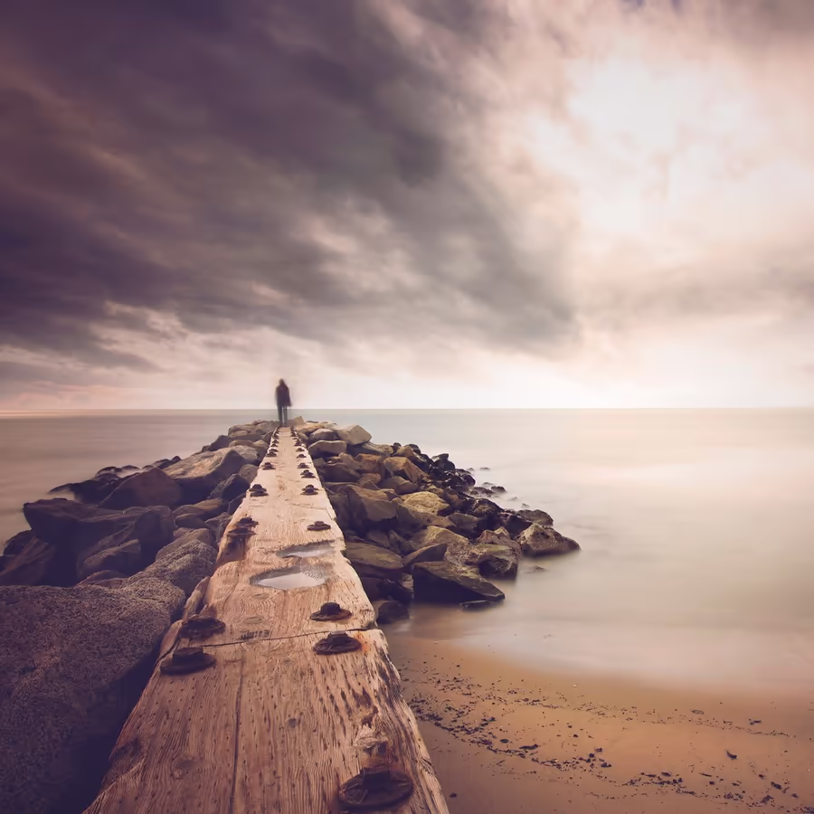 Человек стоит на пирсе глядя вдаль в бурю