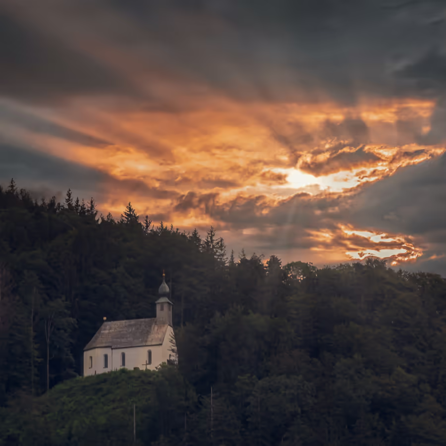 Небольшая церковь одиноко стоящая среди леса под драматическим закатным небом