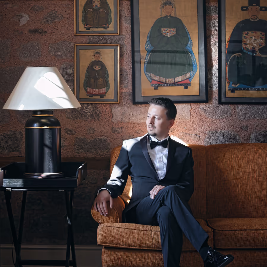 Мужчина в классическом смокинге сидит на диване в интерьере с портретами