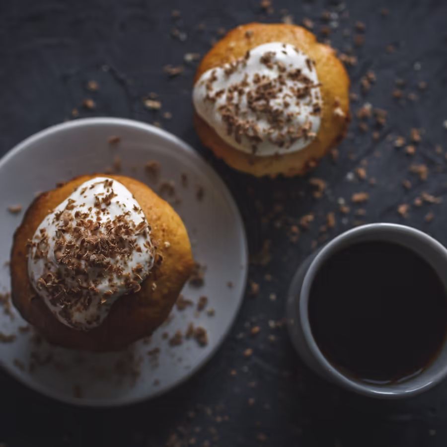 Аппетитные кексы украшенные воздушными сливками и тертым шоколадом рядом чашка черного кофе