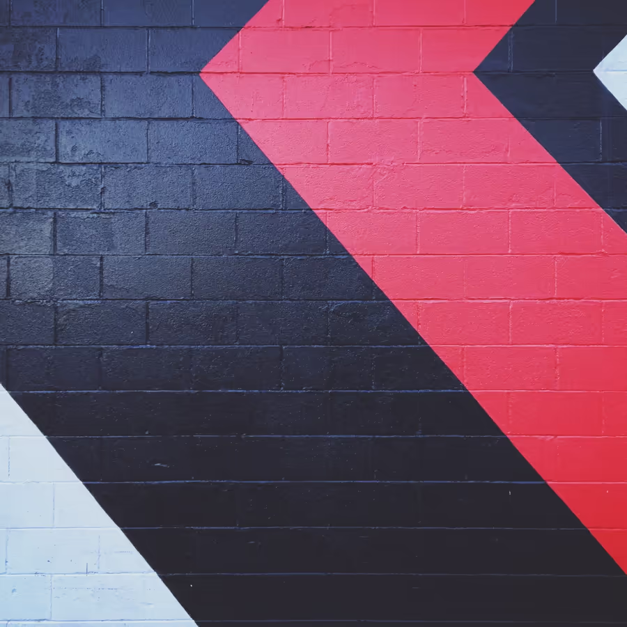 Яркая стрелка направленная вправо на фоне темно-синей и белой кирпичной кладки