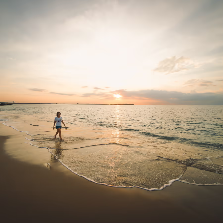 Ребенок идет по волнам на фоне заката