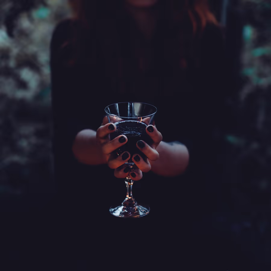 Руки держат бокал с красным вином в полумраке