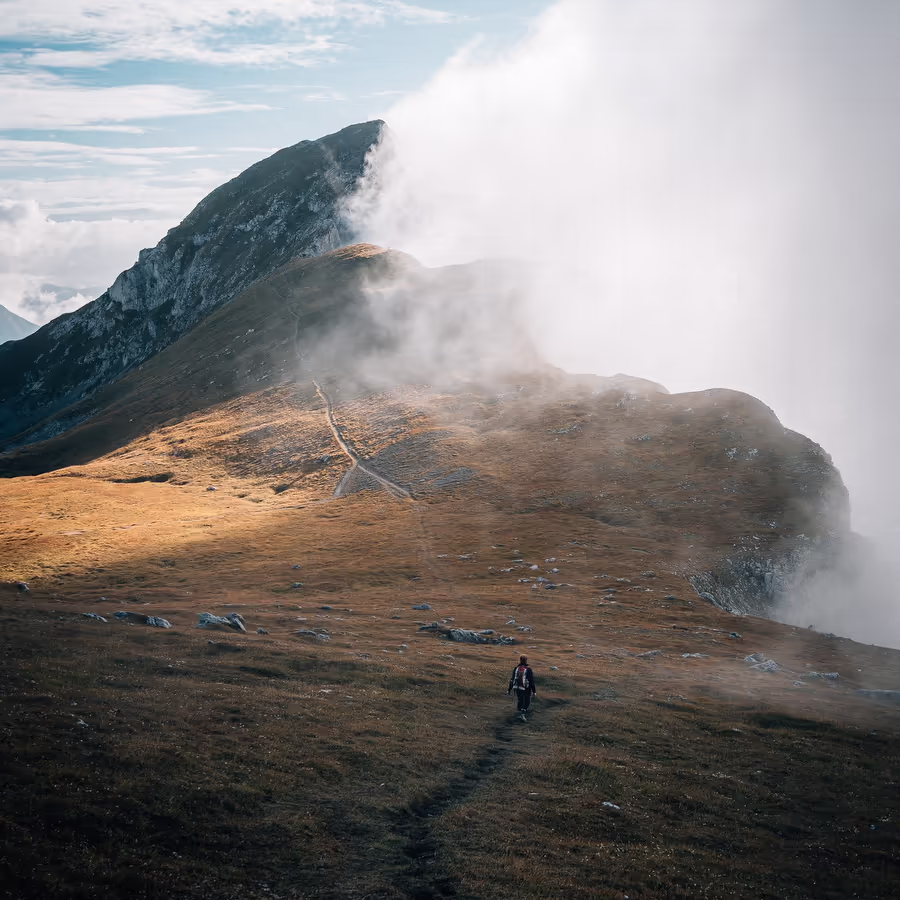 Человек идет по горной тропе под облаками