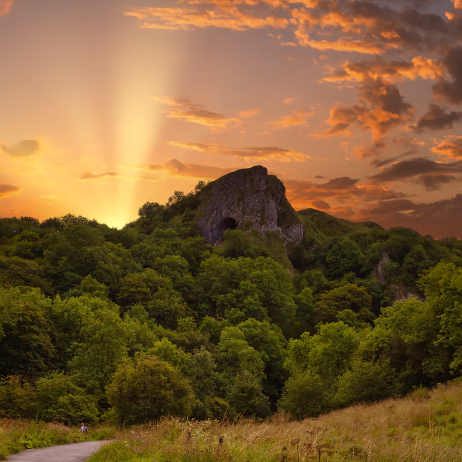 Живописный закат освещает скалистый холм покрытый густым лесом