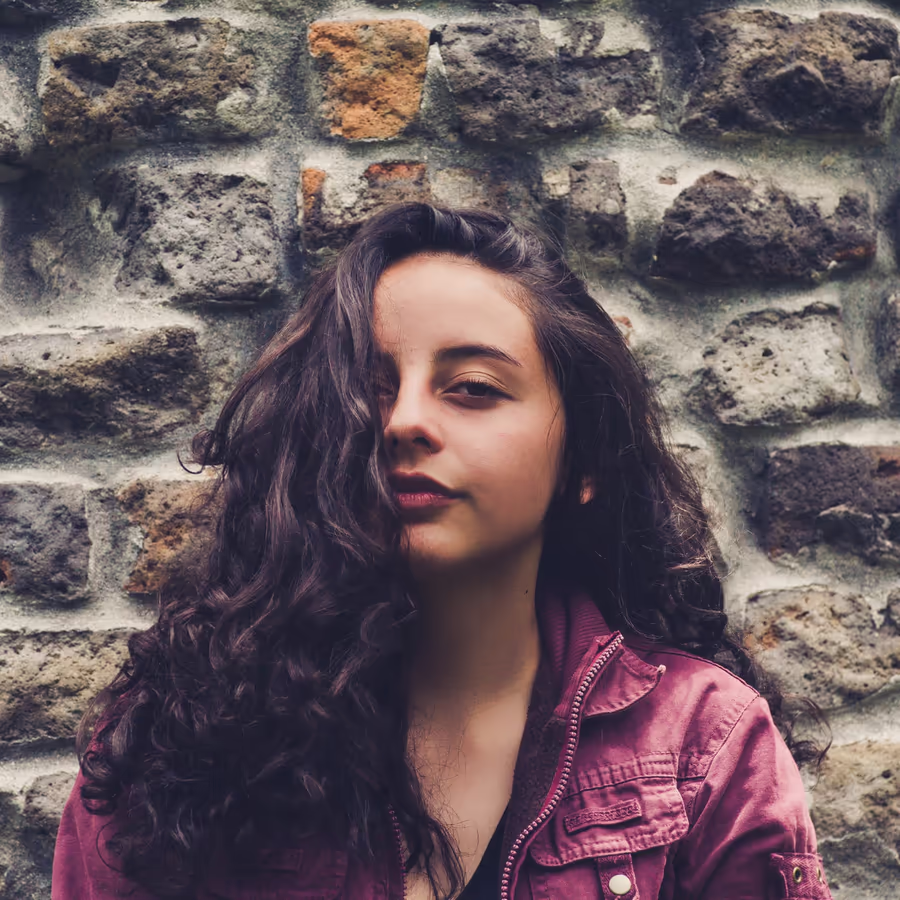Портрет молодой девушки с волнистыми темными волосами на фоне старинной кирпичной кладки