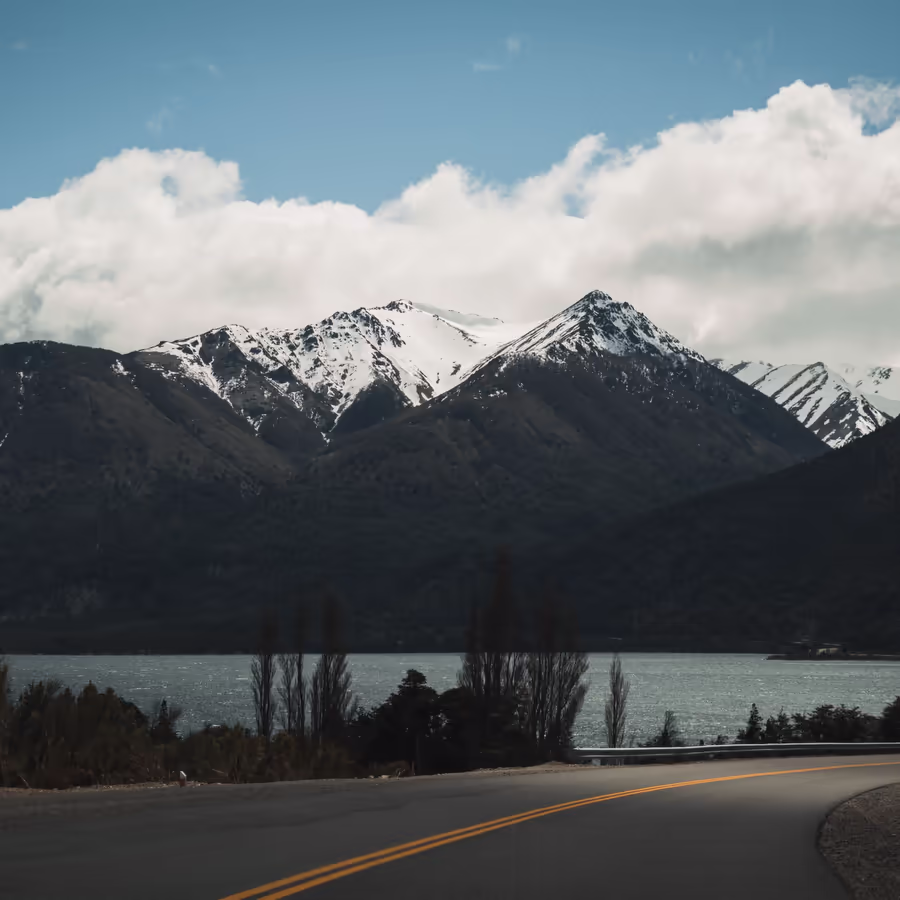 Живописный пейзаж с заснеженными вершинами гор отражающимися в спокойных водах озера На переднем плане - извилистая дорога