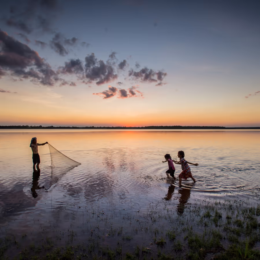 Трое детей играют в воде во время заката солнца