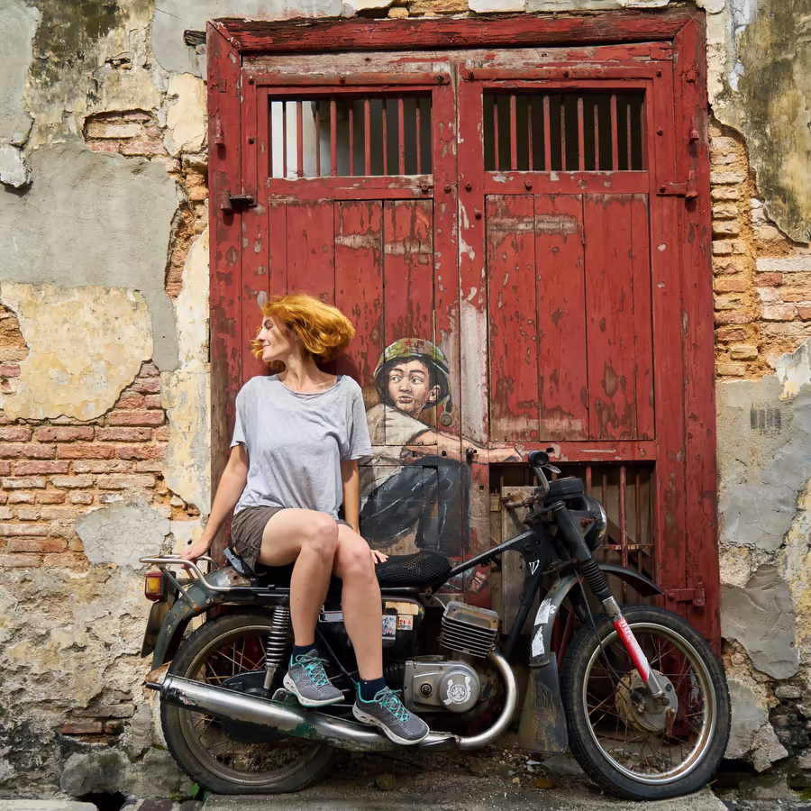 Туристка сидит на мотоцикле возле стены с красочным граффити