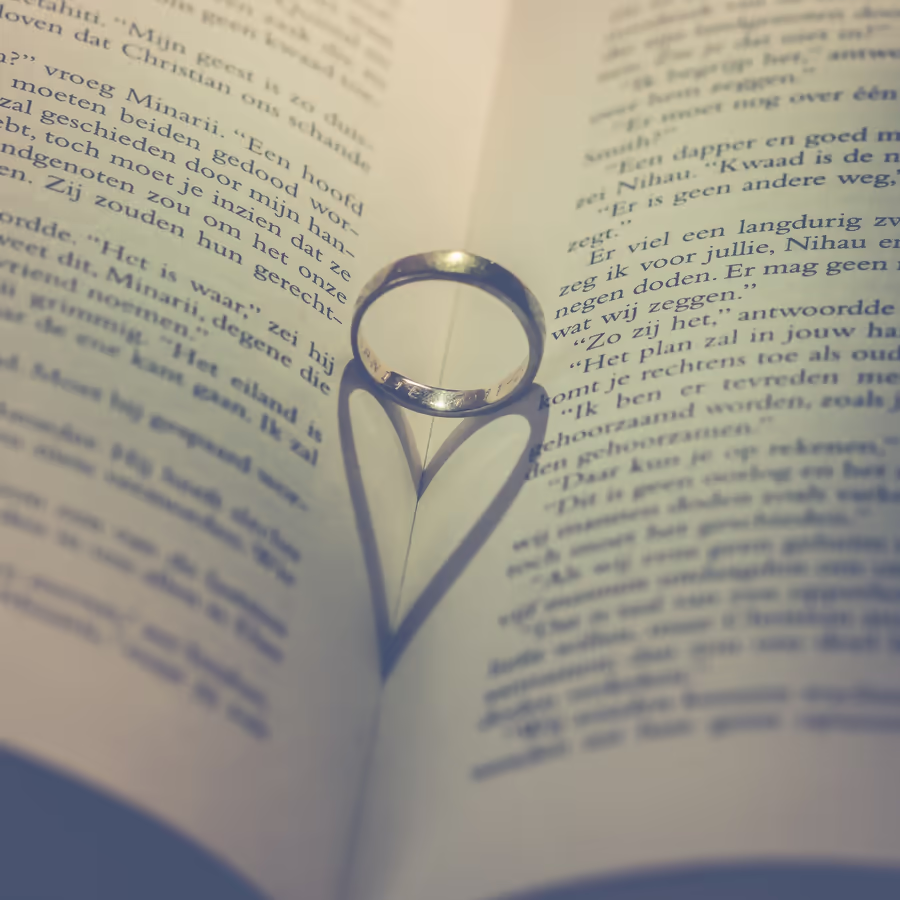 Два золотых обручальных кольца образующие сердце на фоне старинной книги