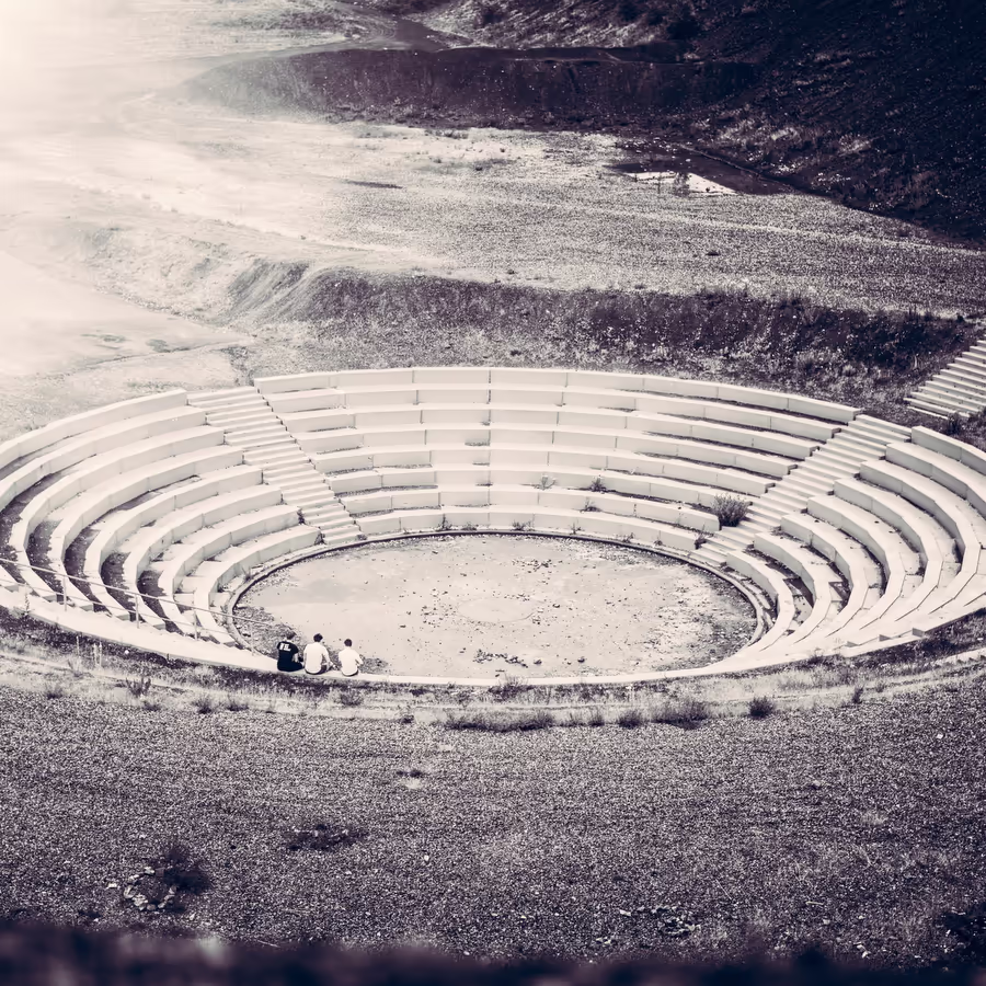Два человека сидят в огромном амфитеатре расположенном посреди бесплодной местности