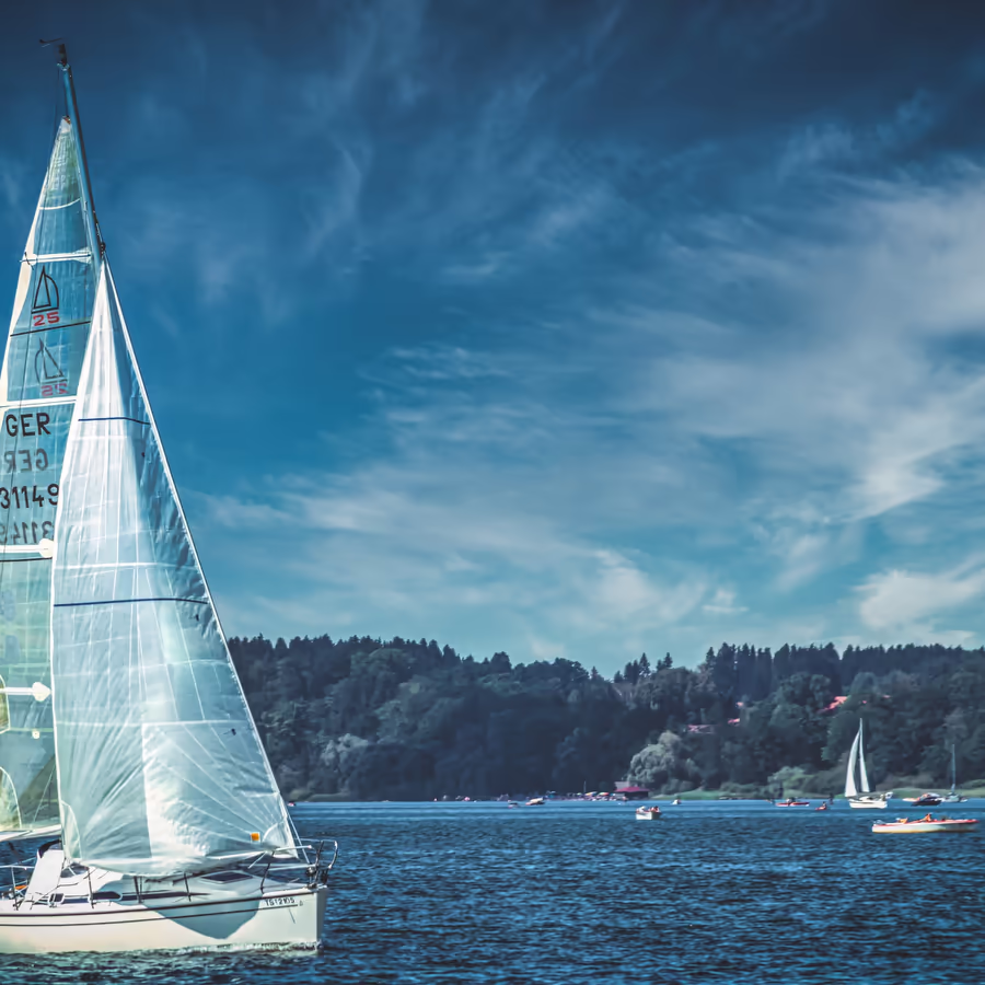 Белые парусники скользят по спокойным водам озера под голубым небом
