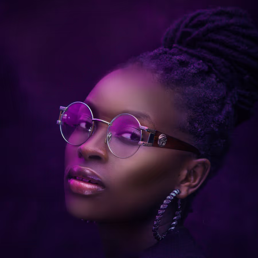 Молодая женщина в круглых очках с необычной прической освещенная пурпурным светом